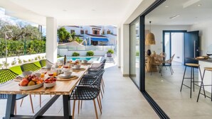 A modern dining area with a pool view, a kitchen with bar seating, and a glass door leading to a balcony. - Ca na Cati by Interhome (Alcúdia)