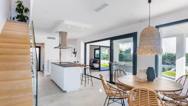 A modern kitchen with a central island, dining area with wicker chairs, and a staircase. - Ca na Cati by Interhome (Alcúdia)