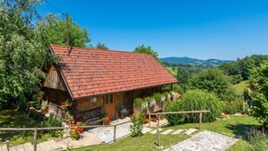 Un chalet en bois avec un toit recouvert de tuiles rouges, entour é d’une végétation luxuriante et accessible par un sentier de pierres menant à l’entrée.
