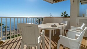 A balcony with a white table and chairs, overlooking the sea.