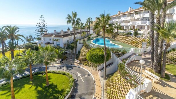 A resort with a pool, palm trees, and a view of the sea.