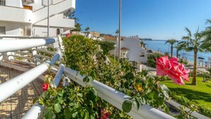 A coastal building with balconies overlooking the sea, a street lamp, and a rose bush in the foreground.
