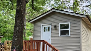 A small, single-story cabin with a front porch and a door, surrounded by trees. - ScrappyJax Cozy Cabin #4 (Glenwood)