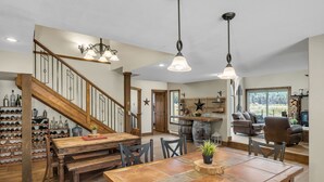 Amplia sala de estar con una escalera de madera, una mesa de comedor con sillas y una zona de cocina con barra.