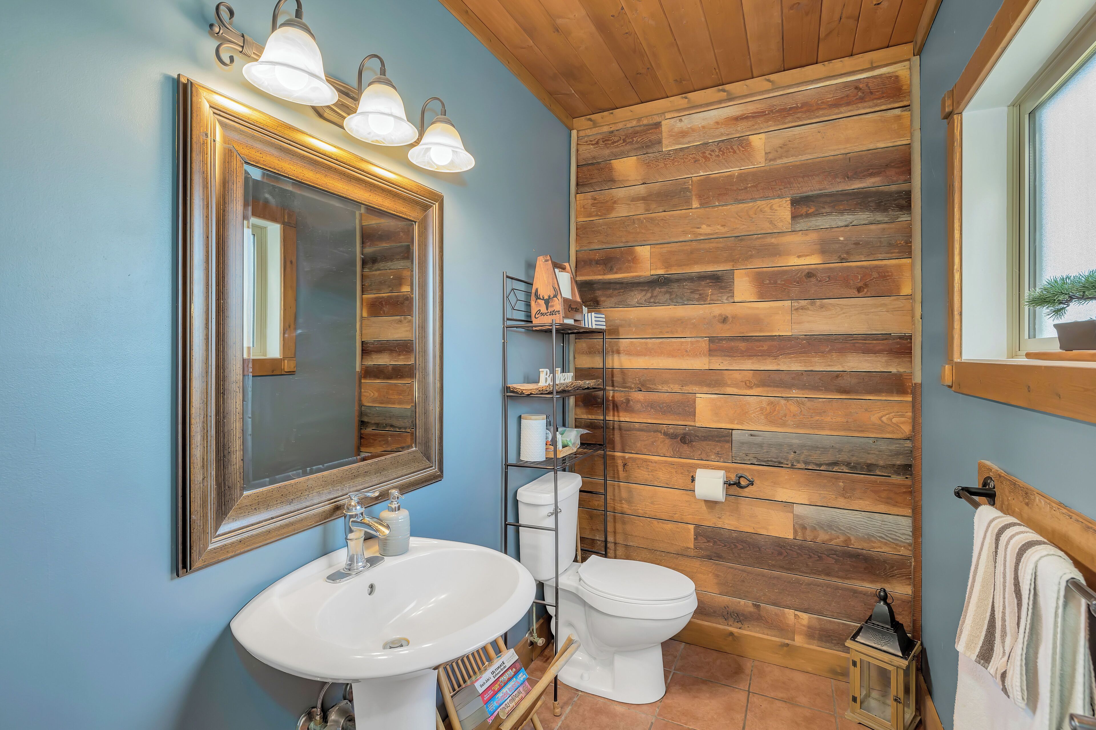 A bathroom with a wooden wall, a white sink, a toilet, and a mirror with lights.