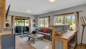 Un salón amplio con una mesa de centro de madera, un sofá con un cojín rojo, y vistas al exterior a través de amplios ventanales.