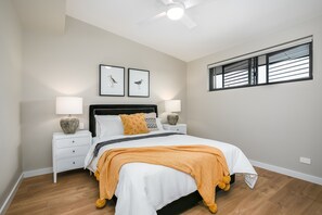 Ein Schlafzimmer mit Bett, Nachttischen, Wandbildern und einem Fenster mit Jalousien.