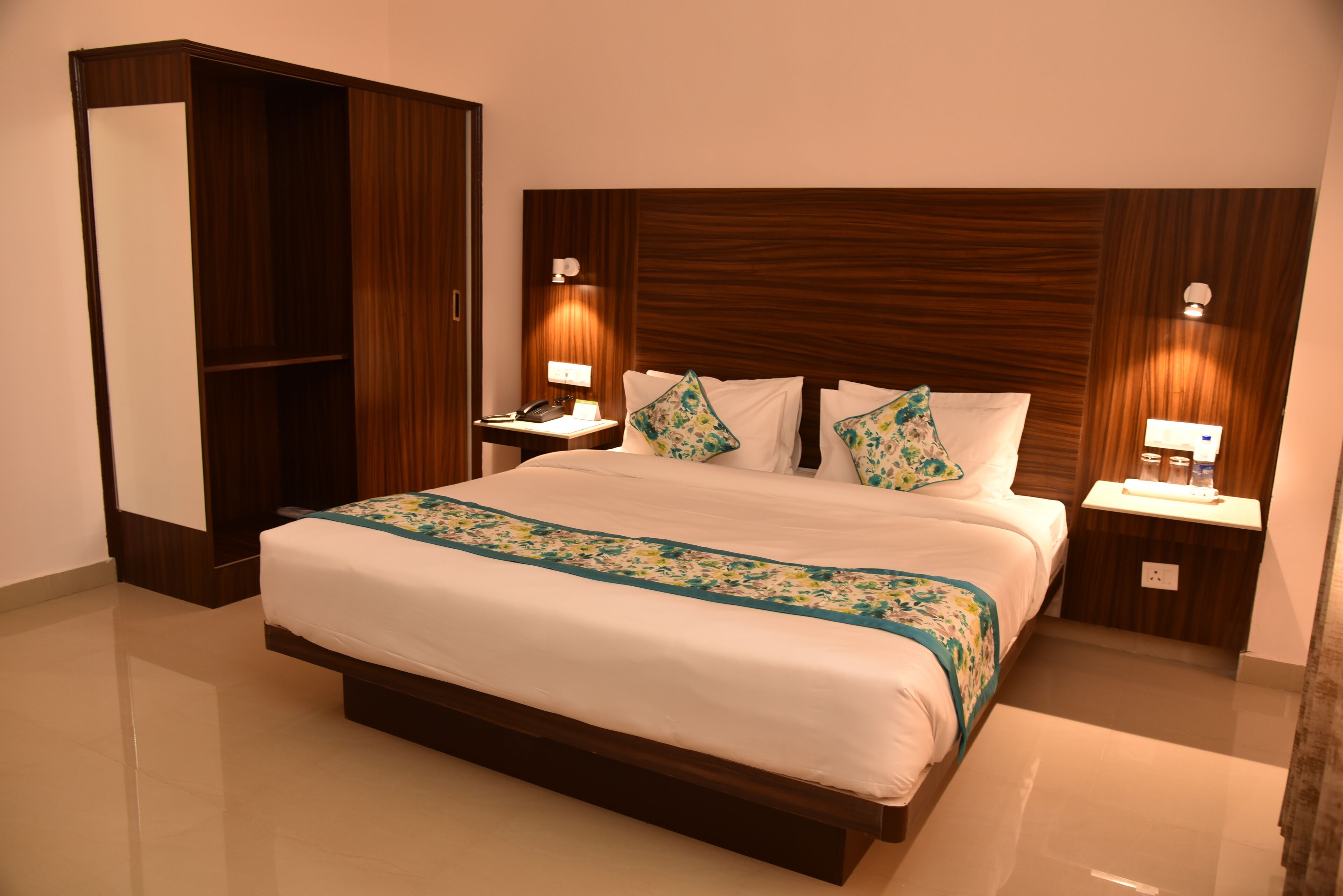Habitación de hotel con una cama grande, cabecero de madera, dos mesitas de noche con lámparas y un armario.