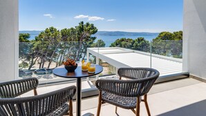 Un balcon avec des fauteuils en osier, une table sur laquelle se trouve un saladier rempli de nourriture et de boissons, et une vue sur la mer et les arbres.