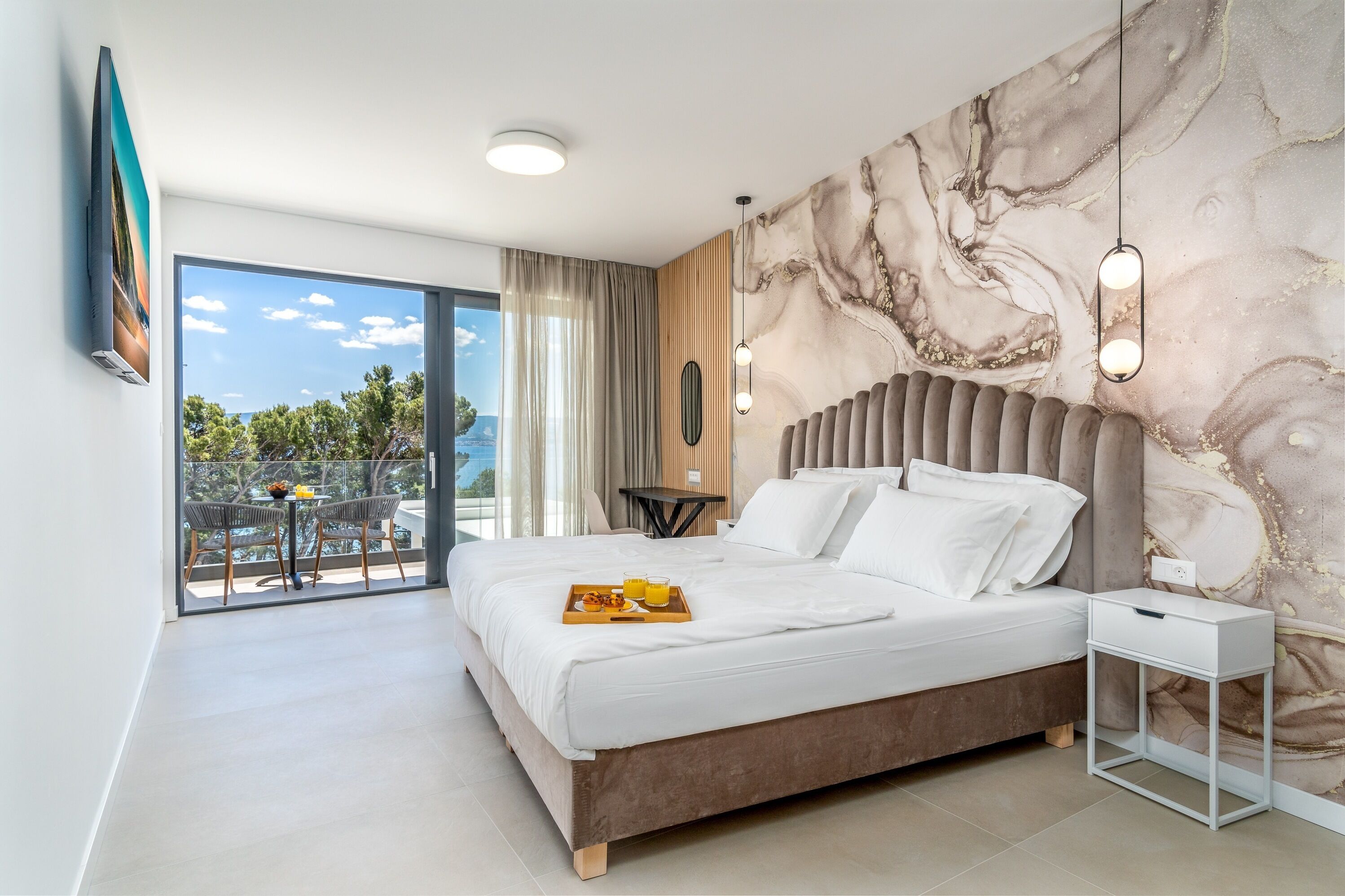 Une chambre d’hôtel moderne dotée d’un grand lit, d’un balcon avec coin salon extérieur et d’un mur en marbre.