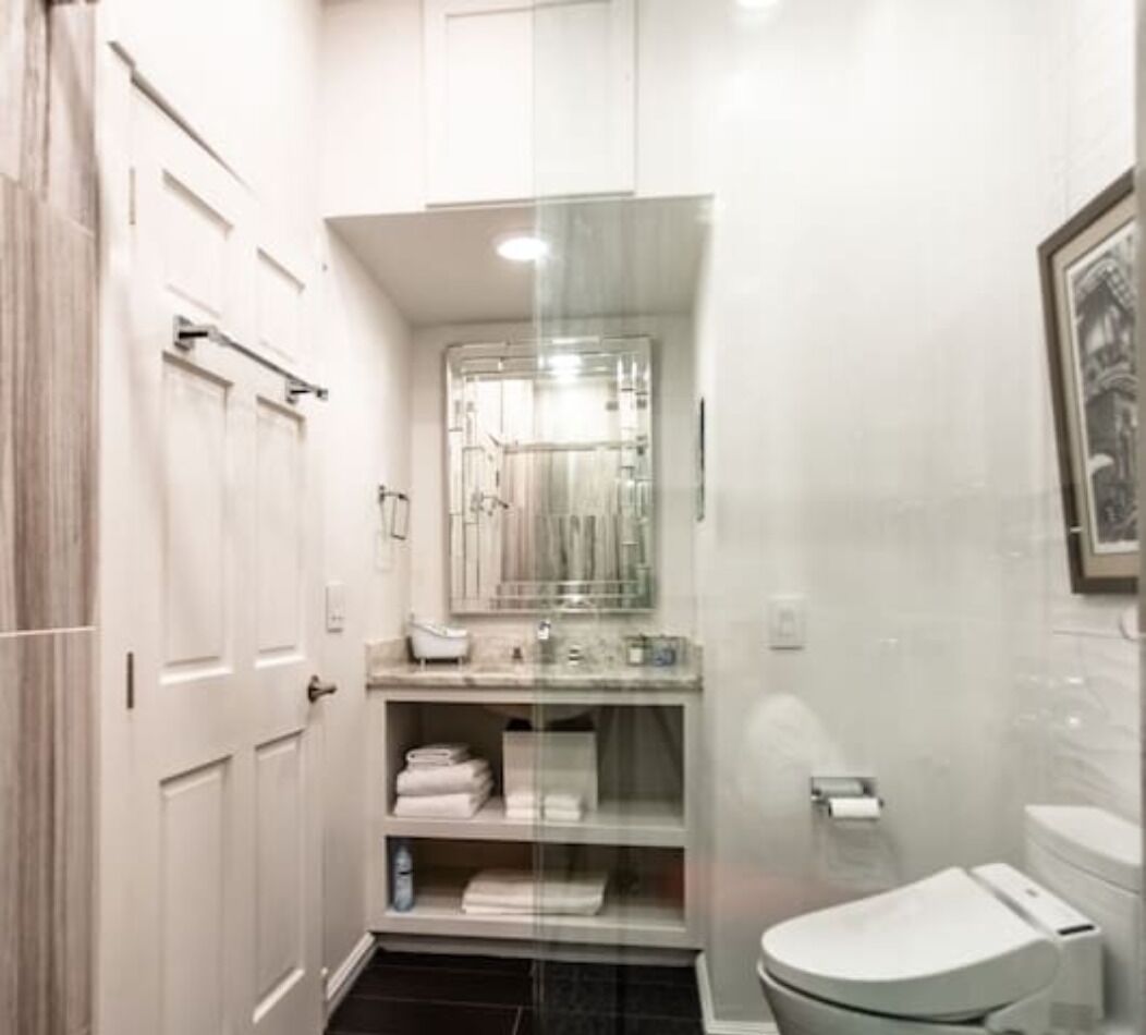 A bathroom with a toilet, sink, and mirror. There are towels and a shelf with toiletries.