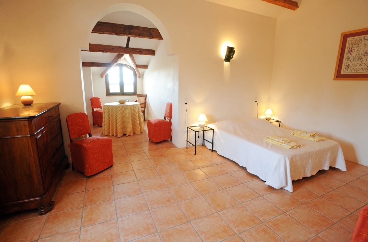 A room with a bed, a small table, a chair, a wooden cabinet, and a window.
