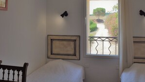 A bedroom with two single beds, a window with a view of a garden, and a wooden ceiling beam. - Le Hameau Montplaisir, its 4 houses, 36 beds and 2 large swimming pools! (Béziers)