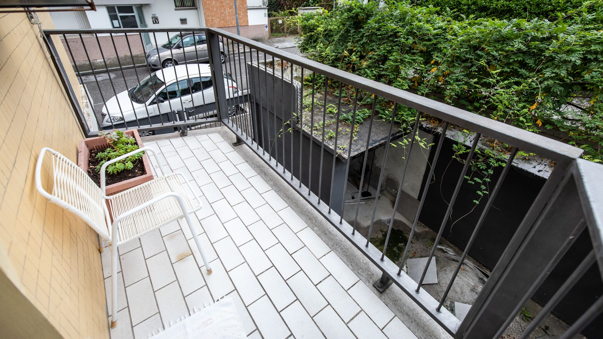 A balcony with a white chair, a small potted plant, and a metal railing.