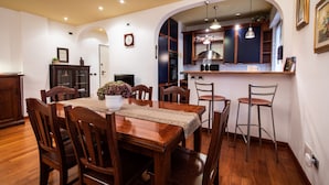 A dining area with a wooden table and chairs, a potted plant, and a kitchen visible through an archway. - Italianway - Gradisca 8 (Udine)