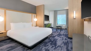 A hotel room with a large bed, a desk, a chair, and a television.