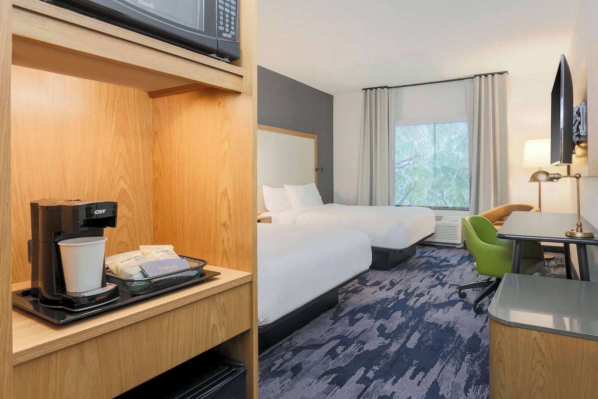 A hotel room with a bed, a desk with a lamp, a coffee machine, and a window with curtains.