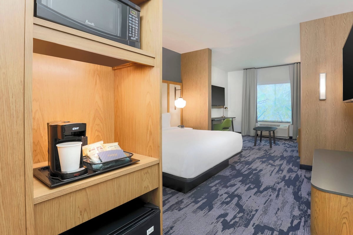 A hotel room with a bed, a desk with a coffee maker, a microwave, and a window with curtains.