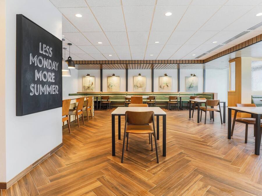 A spacious dining area with wooden flooring, multiple tables and chairs, and a wall-mounted sign.