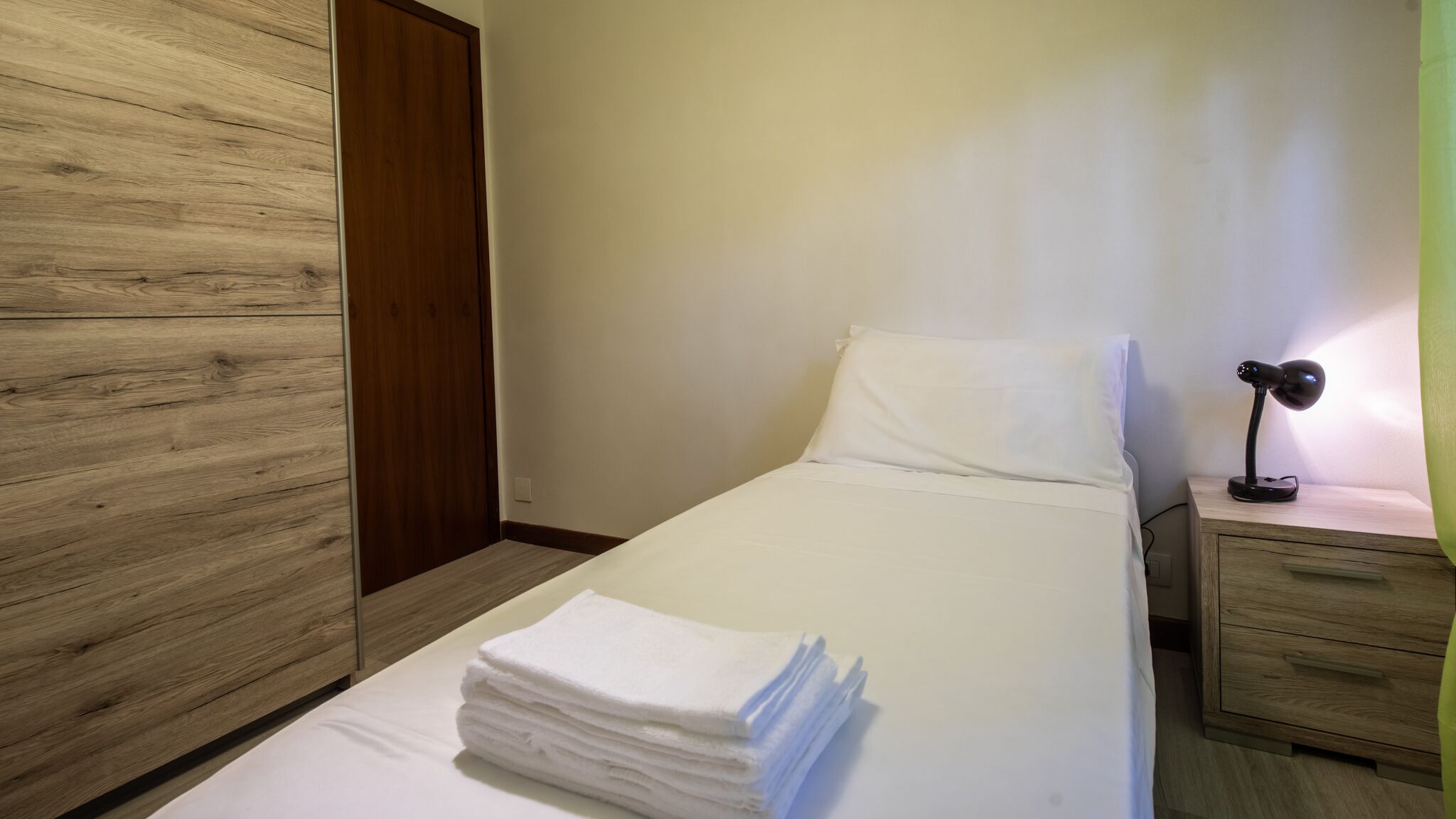 Una cama bien hecha con sábanas blancas y una pila de toallas dobladas.