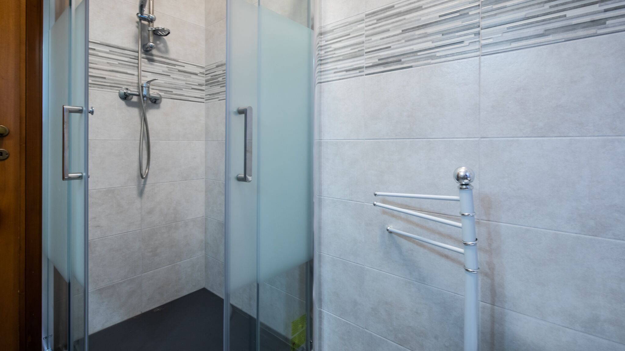 A modern bathroom with a glass shower enclosure, a towel rack, and a glass door.