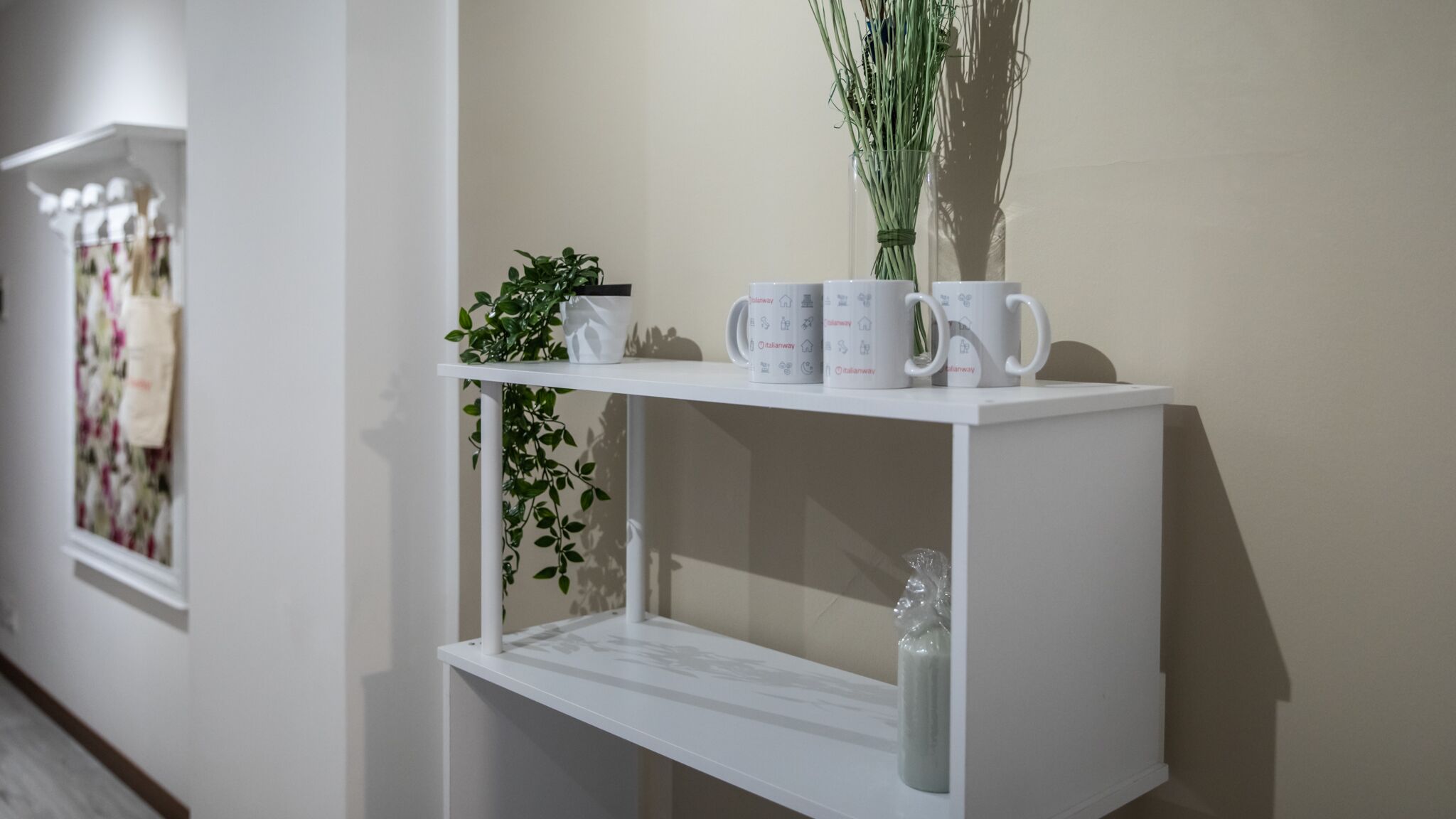 A white shelf with a potted plant, a vase, and several mugs with a logo.