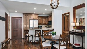 A modern kitchen with wooden cabinets, a central island, and a dining area with chairs.
