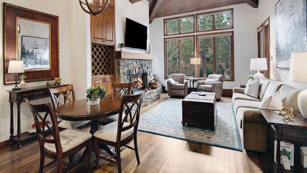 A spacious living room with a fireplace, large windows, and a dining area with wooden furniture.