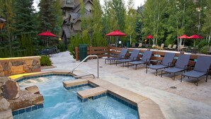 A hot tub area with lounge chairs and umbrellas, surrounded by stone walls and trees.