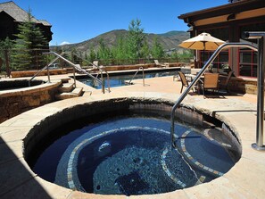 A hot tub surrounded by stone steps and railings, with outdoor seating and a mountain view in the background. - BC Landing 202 | Remodeled 3BR Ski-In/Ski-Out, Summer AC (Beaver Creek)