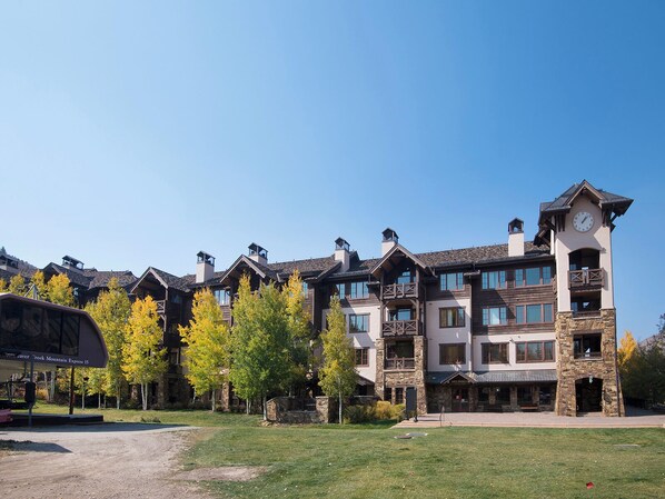 A multi-story hotel with a stone tower and a clock, surrounded by trees and a clear sky. - BC Landing 202 | Remodeled 3BR Ski-In/Ski-Out, Summer AC (Beaver Creek)