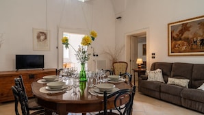 A dining area with a round table set for six, surrounded by chairs. A television is mounted on the wall above the table. - Italianway - Casa del Barone (Lecce)