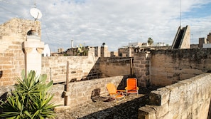 A rooftop terrace with stone walls, a satellite dish, and two orange chairs.