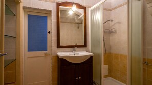 A bathroom with a sink, mirror, shower, and a door with a blue-tinted window.