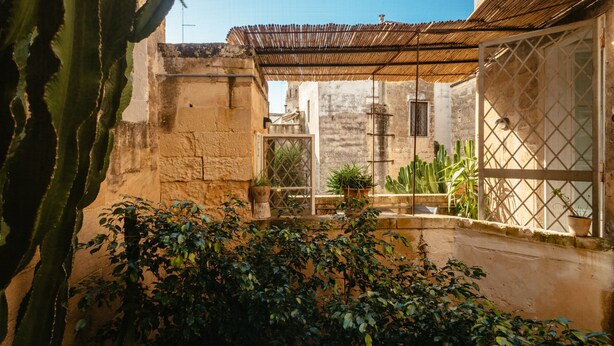 A courtyard with a rustic stone wall, a wooden pergola, and potted plants. - Italianway - Casa del Barone (Lecce)