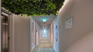 Un pasillo con techo verde artificial, suelo alfombrado y un cartel con los números de las habitaciones en la pared.