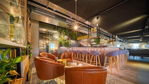 Zona de bar moderna con sillones de cuero, mostrador de bar y plantas.