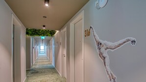 Un pasillo de hotel con un mural de pared verde, puertas numeradas y piso alfombrado.