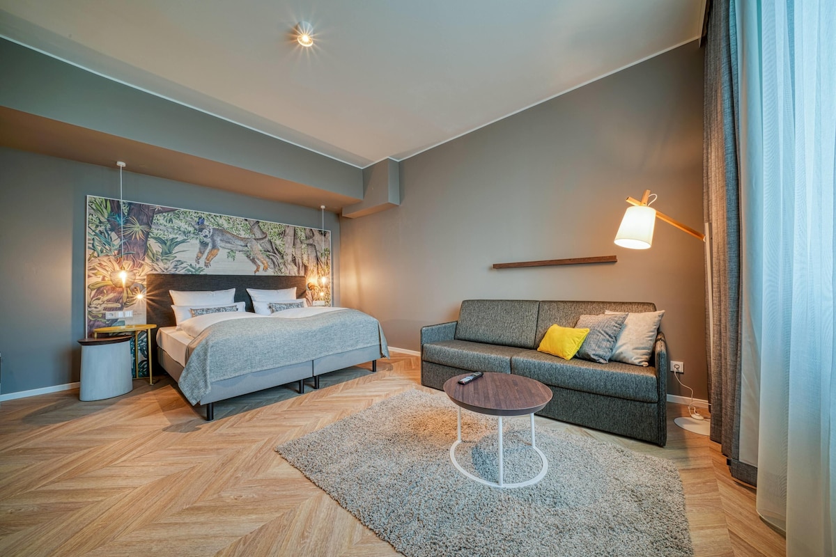 Un dormitorio moderno con cama, sofá, una mesita y una lámpara de pared.