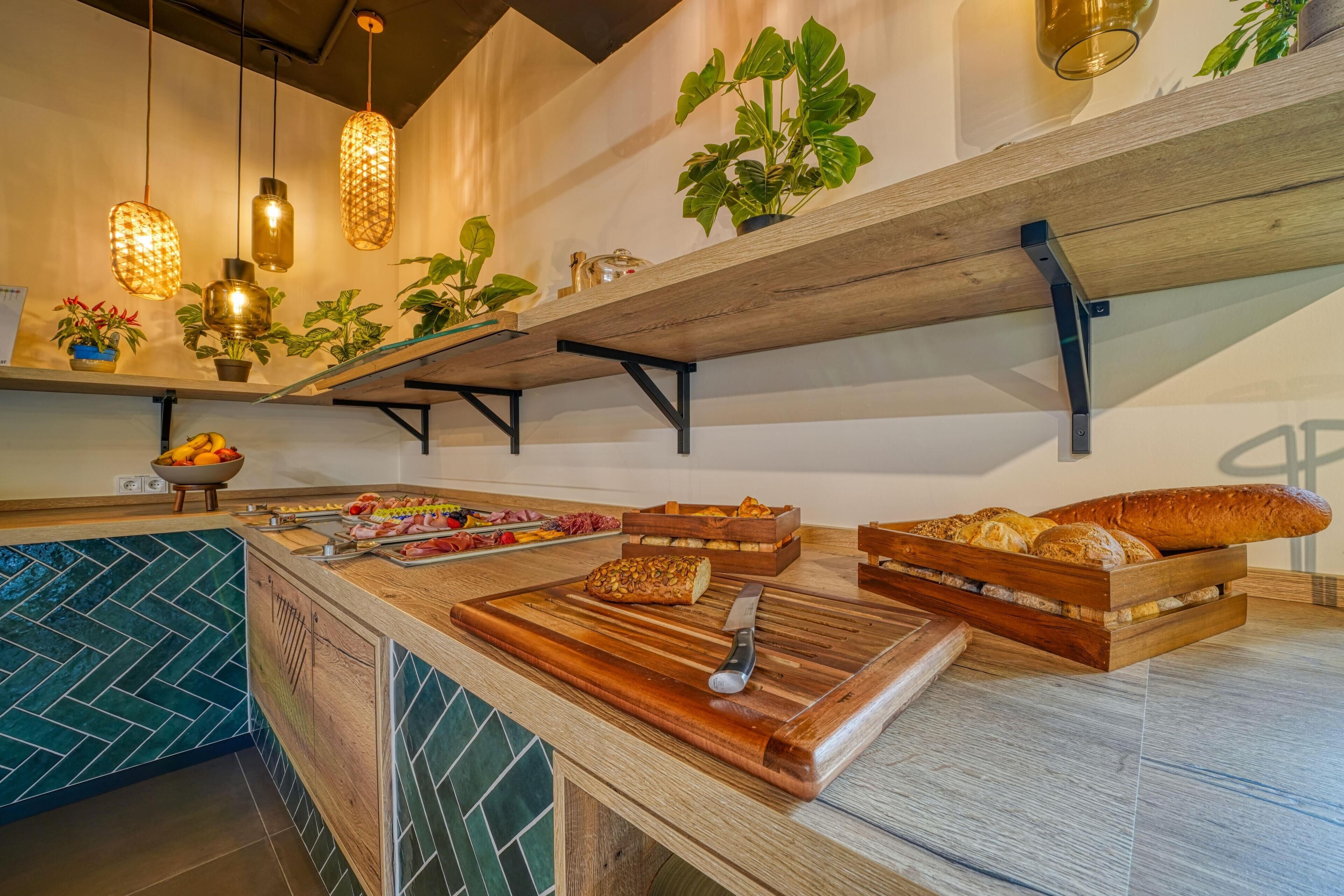 A kitchen counter with bread, a knife, and a cutting board. There are hanging lights and potted plants on shelves above.