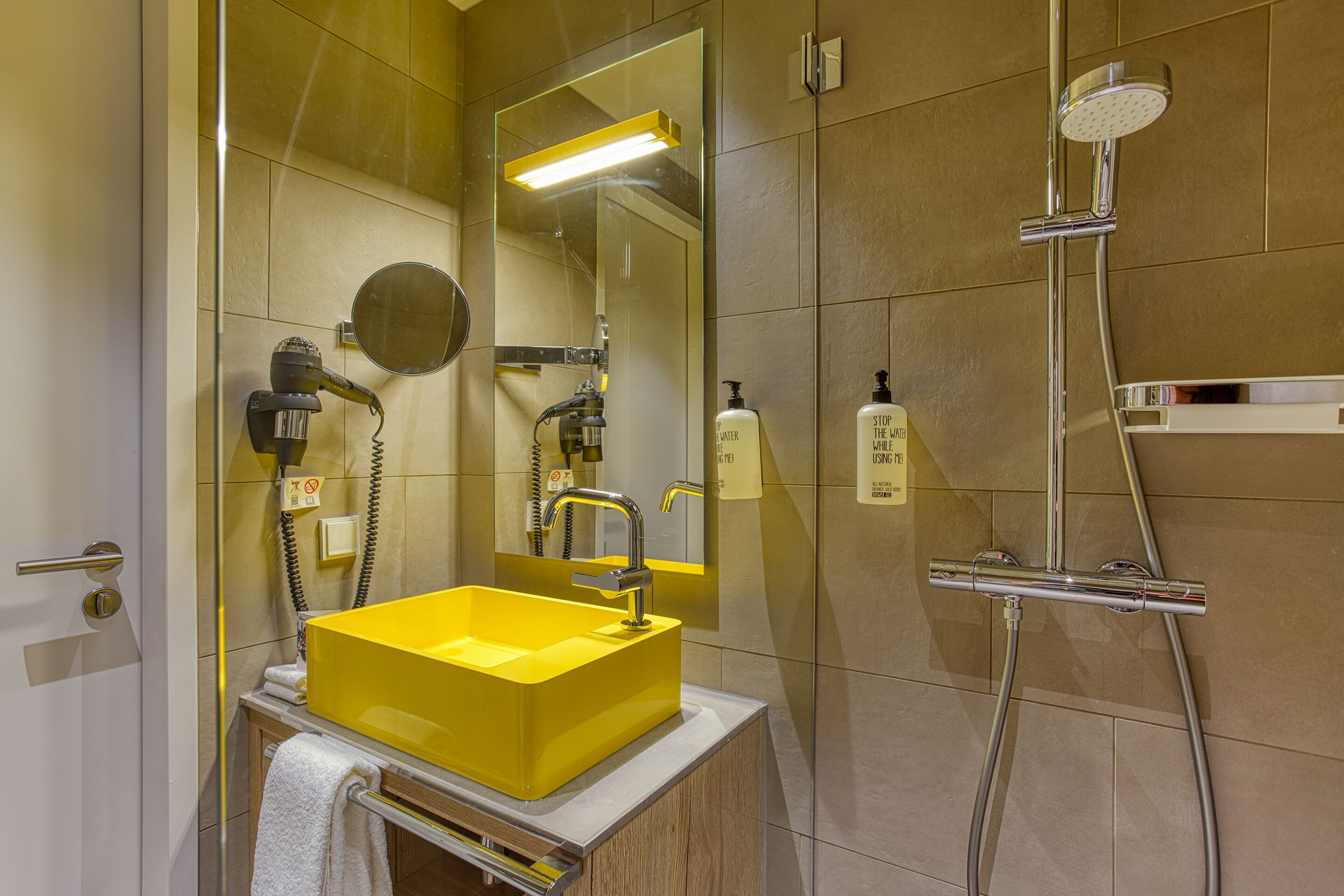 Een moderne badkamer met een geel wastafel, een spiegel, een handdouche en een handdoekrek.