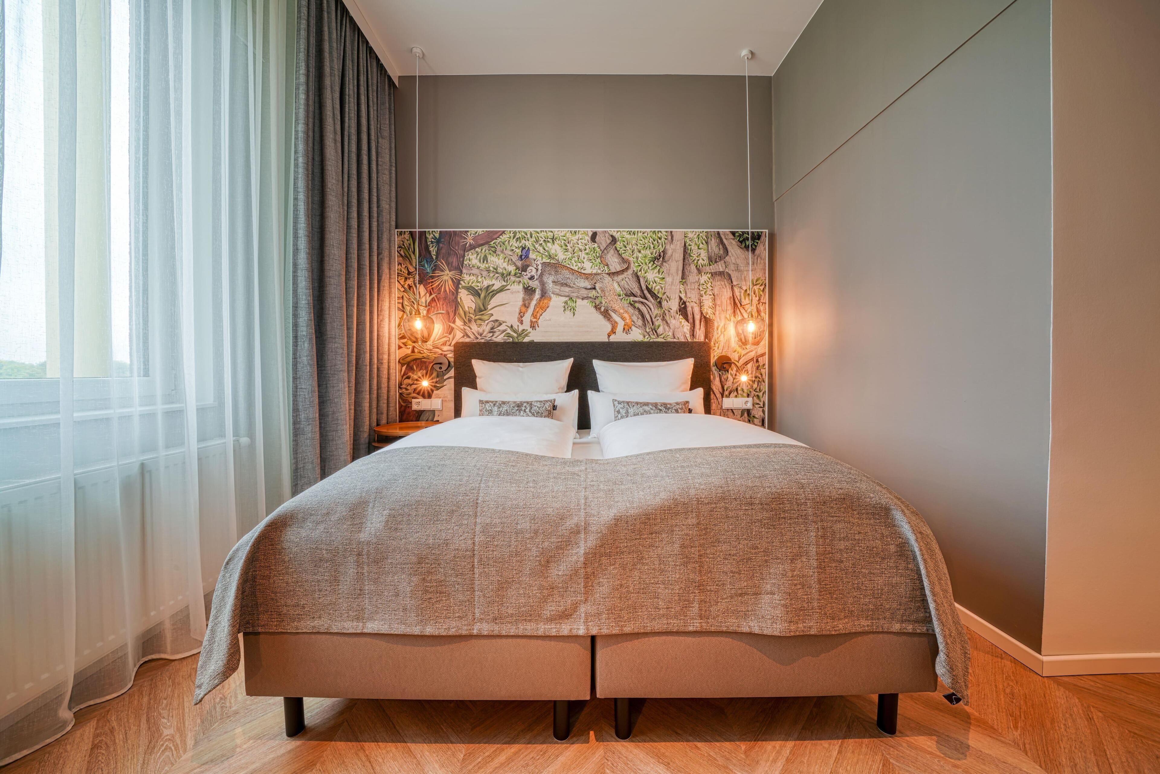 A modern bedroom with a large bed, a mural on the wall, and a view of the outdoors.