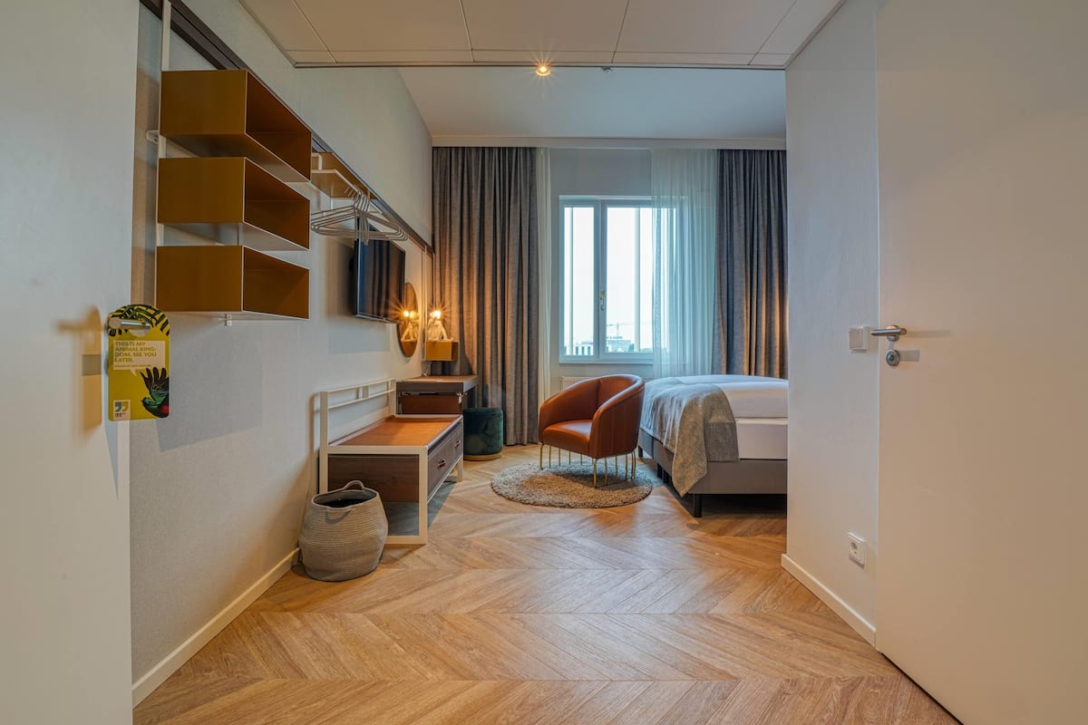 Een hotelkamer met een bed, een stoel, een bureau, een televisie en een raam met gordijnen.