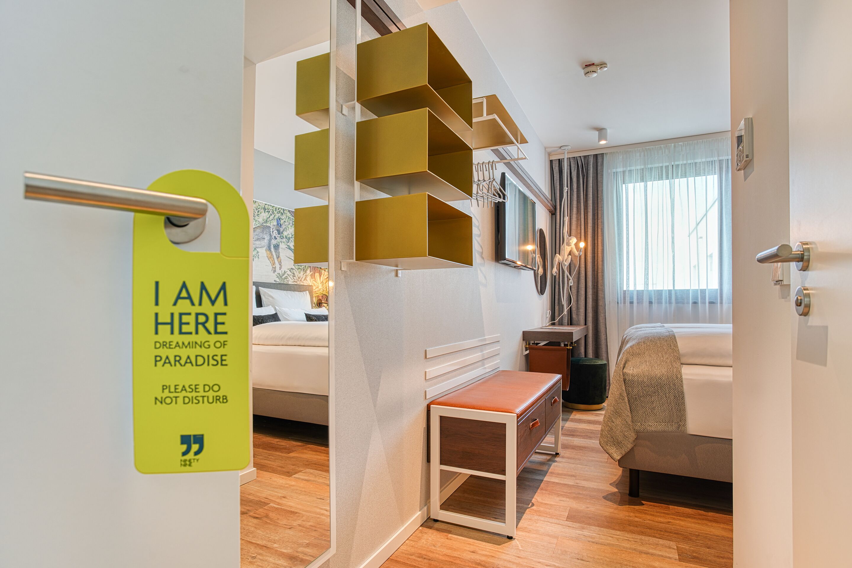 Una habitación de hotel moderna con una cama, un banco y una estantería original.