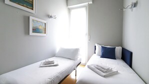 A small, bright room with two single beds, white bedding, and a painting of a coastal scene. - Italianway - Dogali 17 (Santa Margherita Ligure)