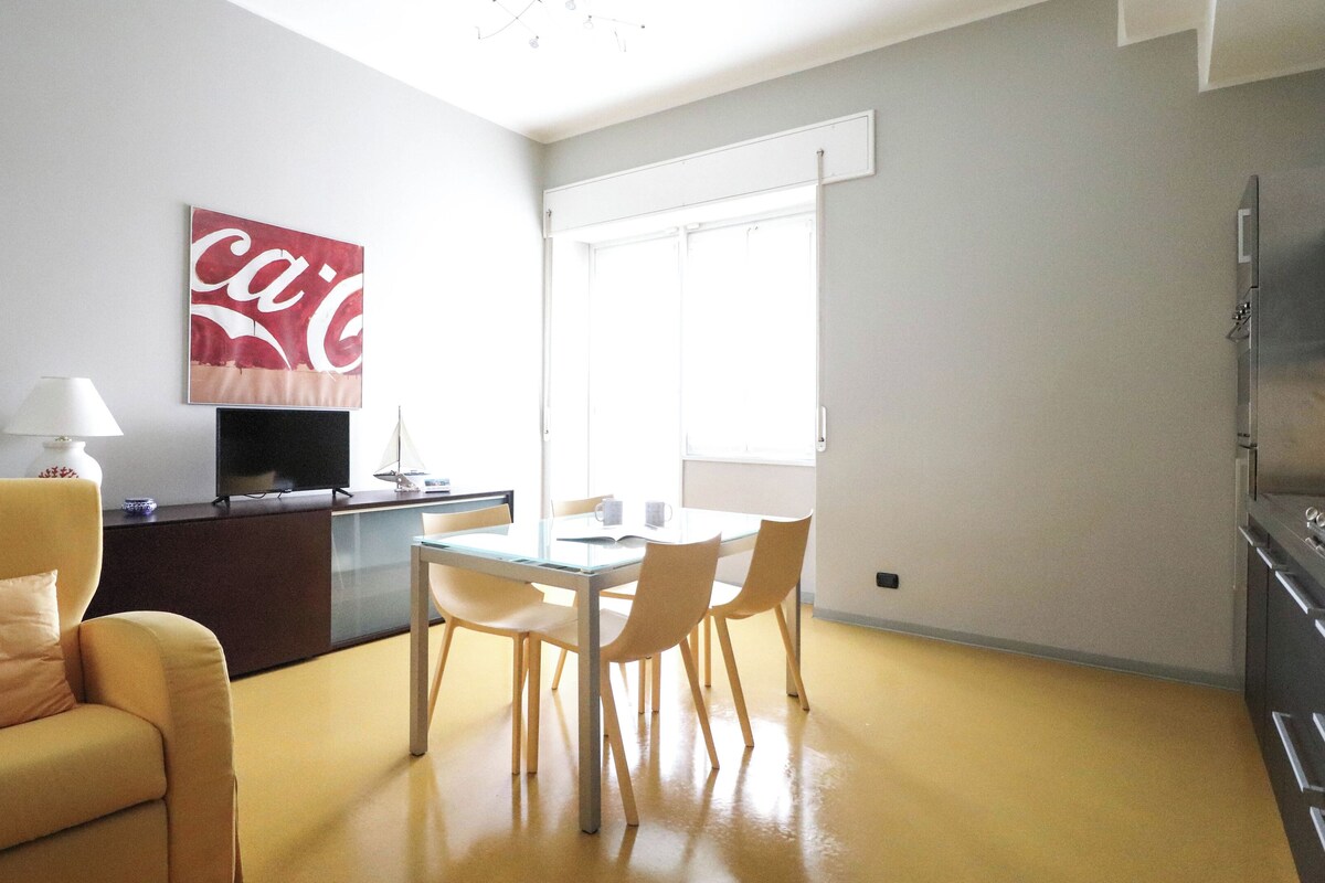A compact living space with a sofa, a dining table with chairs, a TV, and a kitchen area with a stove.