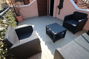 An outdoor patio with wicker furniture, a potted plant, and a door. - Marcopolo-Terrace (Venice)