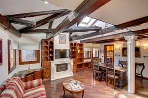 A spacious living room with exposed wooden beams, a fireplace, a television, and a dining area with wooden furniture. - Marcopolo-Terrace (Venice)