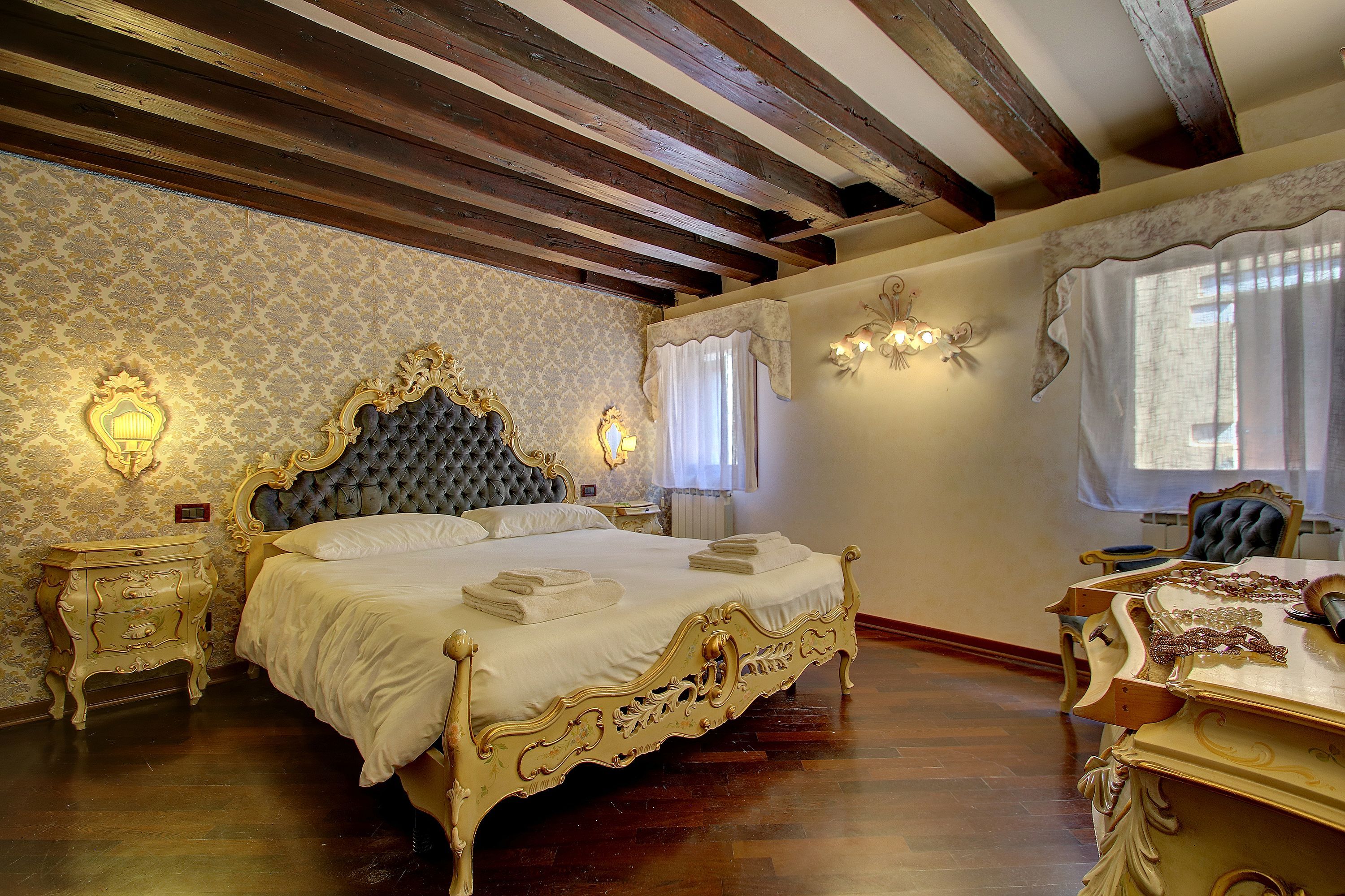 A room with a large ornate bed, wooden beams on the ceiling, and a chandelier.