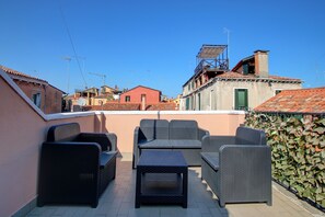 A rooftop terrace with wicker furniture, a view of surrounding buildings, and a clear blue sky. - Marcopolo-Terrace (Venice)
